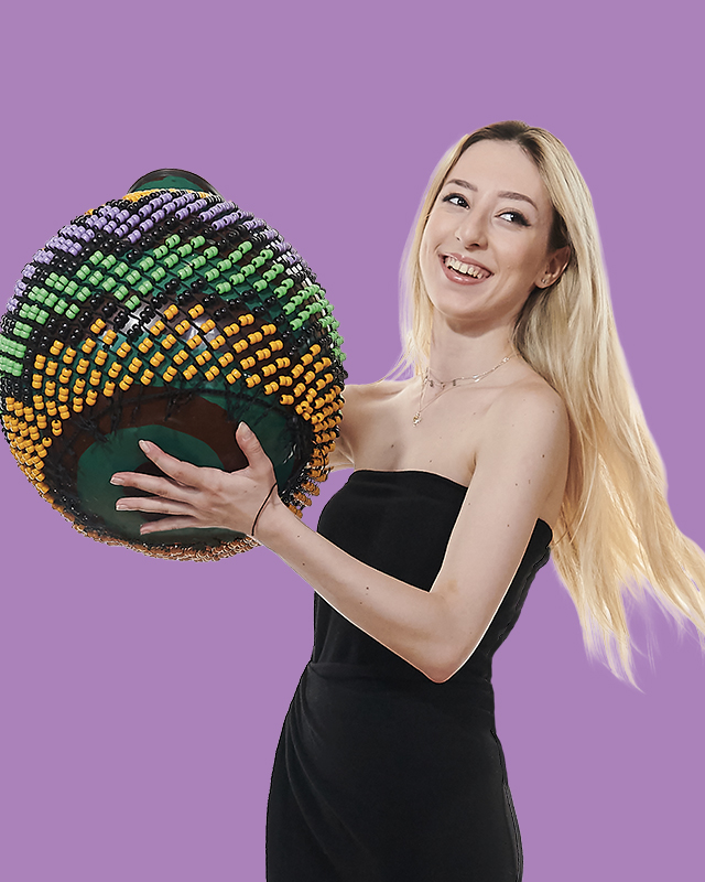 A female student, wearing a black tube top, shaking a shekere, a type of percussion instrument.